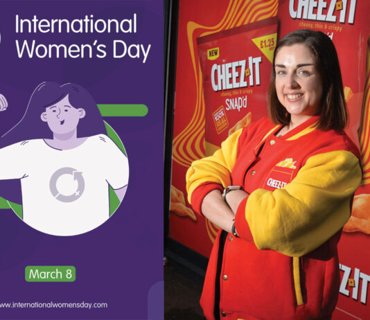 International Women’s Day – Londis Solo Convenience Baillieston Natalie Lightfoot, store owner at Londis Solo Convenience Baillieston, stands wearing a Cheez-It branded jacket with an advert for the brand behind her with a picture of the post for International Women's Day 2025.