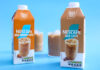 Cartons of Nescafé Iced Latte and Iced Caramel Latte stand against a blue background with the drinks poured out into ribbed glasses behind the cartons with ice.