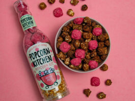 Popcorn Kitchen pops Peter Pigs on the menu A bottle of Popcorn Kitchen Peter Pigs lies down on a pink background with a bowl that has chocolate covered popcorn and pieces of pig shaped strawberry chocolate with both the chocolate and popcorn lying around the bowl as well.