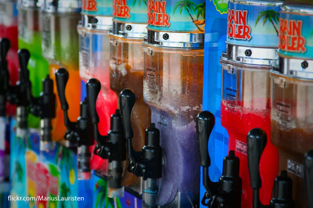 A range of slushie machines with bright colours are lined up containing slushie drinks of different flavours.