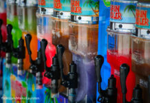 A range of slushie machines with bright colours are lined up containing slushie drinks of different flavours.