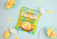 A packet of Swizzels Squashies Drumchick sits on a blue table with baskets filled with the sweets around the packet with small toy eggs around the packet.