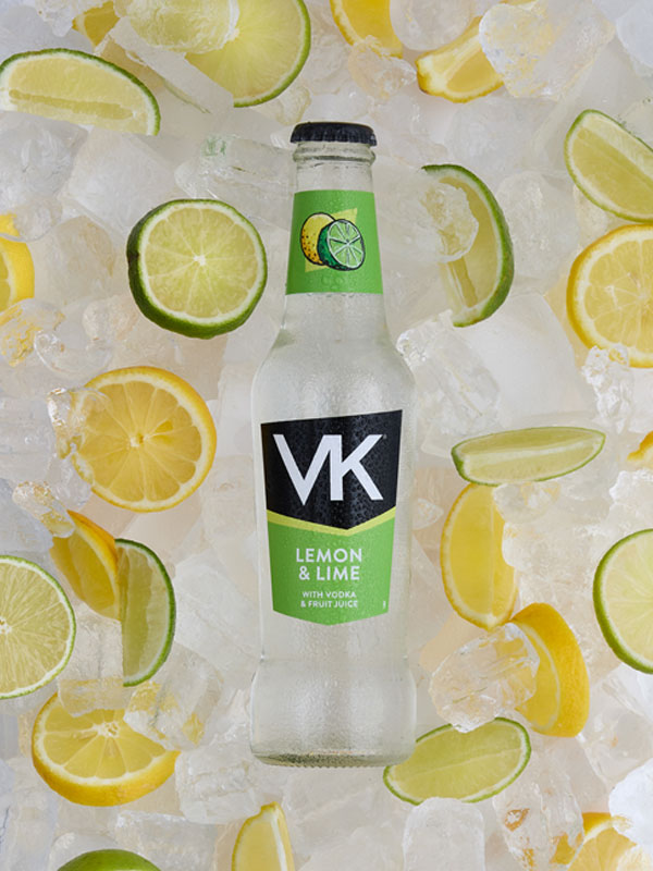 A bottle of VK Lemon & Lime lies on top of a pile of ice with lemon and lime slices.