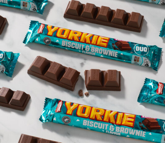 Yorkie unveils new Biscuit & Brownie flavour Packs of Yorkie Biscuit & Brownie chocolate bars lay across a grey surface, with the chocolate bars lying outside the wrapper as well.