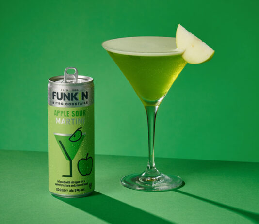 Funkin Cocktails unveils Sour Apple Martini cans A can of Funkin Cocktails Sour Apple Martini stands next to a martini glass with the drink inside it and a slice of green apple garnished on the glass. This is shot against a green background.