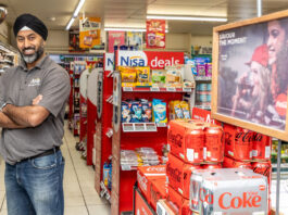 Coca-Cola celebrates convenience stores for 125th year in Great Britain A man stands with his arms folded to the left-hand side of the image of the inside of a convenience store with cans of Coca-Cola and Diet Coke stacked up on the right and promotional material above the cans.
