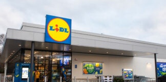 The front of a Lidl store with the discounter's logo on a sign above the glass door entrance.
