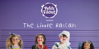 Four children are lined up against a police wall with purple walls as they are covered in mess as though they have been caught by their parents. Each holds a board with their name on it, on the wall behind them is the Petits Filous logo and the text 'The Little Rascals'.