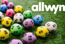 Multi-coloured National Lottery balls lie on grass with the Allwyn logo in the top right hand corner.