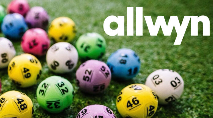 Multi-coloured National Lottery balls lie on grass with the Allwyn logo in the top right hand corner.