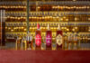 Bottles of The Antiquary whisky are lined up on a bar featuring the 15 Year Old, 21 Year Old and 30 Year Old. Along with these bottles, there are smaller sample bottles for blending as well as whisky glasses to serve in with unlabelled whisky sample bottles on shelves behind the bar.