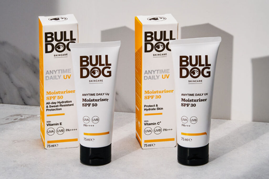 Packs of Bulldog Anytime Daily UV Moisturiser SPF 50 and Bulldog Anytime Daily UV Moisturiser SPF 30 with the tubes of cream standing outside the outer packs on a white table with their shadows casted onto a white wall behind the products.