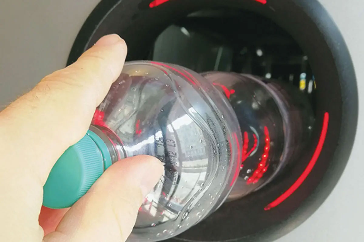 A person is putting an empty plastic bottle into a reverse vending machine.