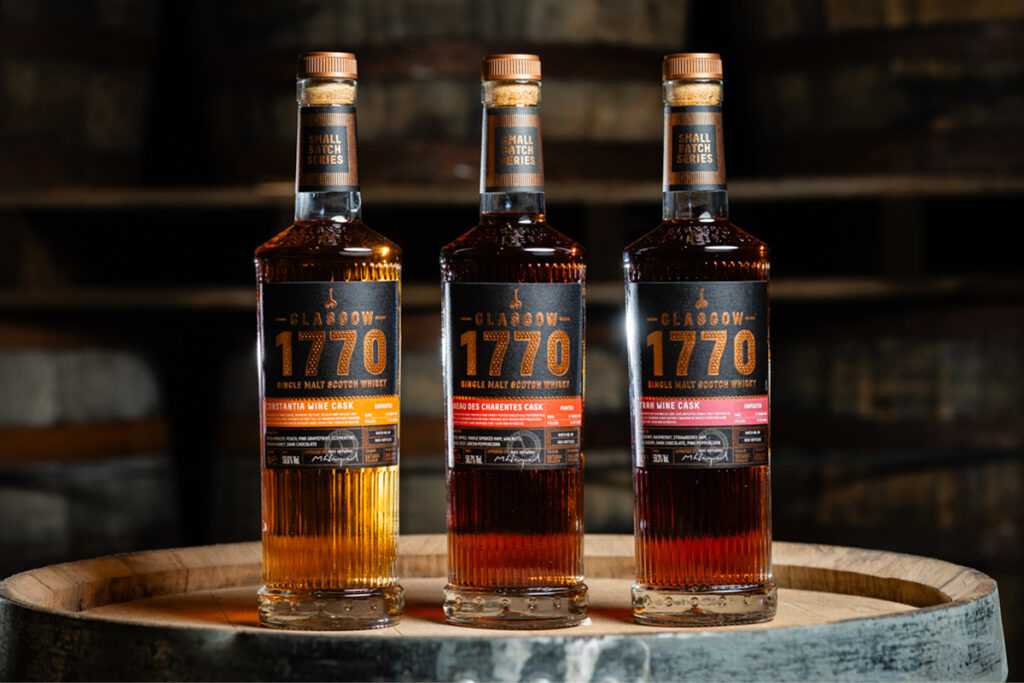 Bottles of Glasgow 1770 Small Batch Series Wine Cask editions including Constantia Wine Cask Matured, Syrah Wine Cask Matured and Pineau des Charentes Wine Cask Matured. All three bottles stand on top of a wooden barrel.