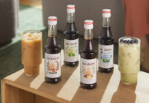 Bottles of Monin Concentrate variants including Cold Brew, Matcha Green Tea, Chai Tea and Blueberry Matcha Green Tea with iced coffee serves in the glasses around them.