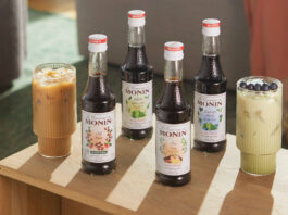 Bottles of Monin Concentrate variants including Cold Brew, Matcha Green Tea, Chai Tea and Blueberry Matcha Green Tea with iced coffee serves in the glasses around them.