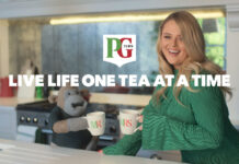 The PG Tips Monkey mascot with comic actor Emily Atack stand in a kitchen with Mr and Mrs Mugs as they go to clink them together. The PG Tips logo is on top of the image with text that reads 'LIVE LIFE ONE TEA AT A TIME'.