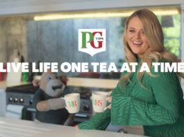 The PG Tips Monkey mascot with comic actor Emily Atack stand in a kitchen with Mr and Mrs Mugs as they go to clink them together. The PG Tips logo is on top of the image with text that reads 'LIVE LIFE ONE TEA AT A TIME'.