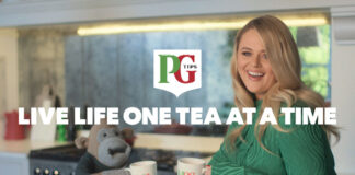 The PG Tips Monkey mascot with comic actor Emily Atack stand in a kitchen with Mr and Mrs Mugs as they go to clink them together. The PG Tips logo is on top of the image with text that reads 'LIVE LIFE ONE TEA AT A TIME'.