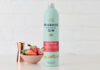A bottle of Penrhos Handcrafted Wonky Strawberry Gin stands on a white table against a white background with a pink bowl of strawberries next to the bottle and a rose gold jigger measure behind the bowl.