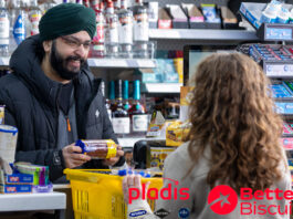 pladis unveils new retailer platform Better Biscuits A man serves a customer at a till point inside a convenience store. The customer has placed a yellow shopping basket onto the counter with items inside it as the retailer takes items out to scan them. The retailer is holding a packet of McVitie's Chocolate Digestives.