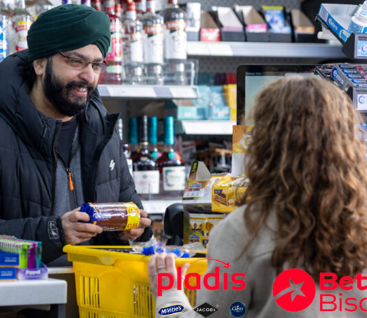 pladis unveils new retailer platform Better Biscuits A man serves a customer at a till point inside a convenience store. The customer has placed a yellow shopping basket onto the counter with items inside it as the retailer takes items out to scan them. The retailer is holding a packet of McVitie's Chocolate Digestives.