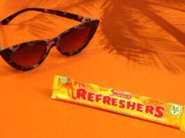 Swizzels celebrates 70 years of Refreshers with new Tropical flavour A bar of Refreshers Tropical lies on an orange floor and wall with sunglasses next to it and the shadow a palm tree behind it.