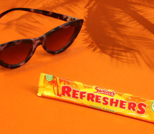 Swizzels celebrates 70 years of Refreshers with new Tropical flavour A bar of Refreshers Tropical lies on an orange floor and wall with sunglasses next to it and the shadow a palm tree behind it.