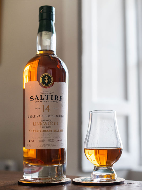 A bottle of Saltire Rare Malt Whisky 14 Year Old Linkwood stands on a table with a nosing glass next to it, the glass has whisky inside it.