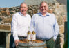 Saltire Rare Malt Founders Nigel Heywood and Keith Rennie (left to right) stand behind a whisky barrel with two whisky bottles on top of the barrel and a nosing glass in front of the whisky bottles.