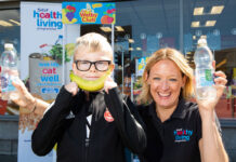 Kathryn Neil, programme director of the Healthy Living Programme, stands next to a child outside Spar Mastrick. Neil holds a bottle of water in each hand and the child holds a banana up to his mouth to look like a smile.