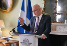 John Swinney, first minister of Scotland, stands at a white podium in Bute House during a press conference.