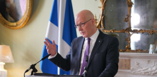 John Swinney, first minister of Scotland, stands at a white podium in Bute House during a press conference.