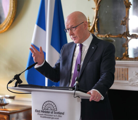 ScotGov sets out pledge to stamp out retail crime John Swinney, first minister of Scotland, stands at a white podium in Bute House during a press conference.