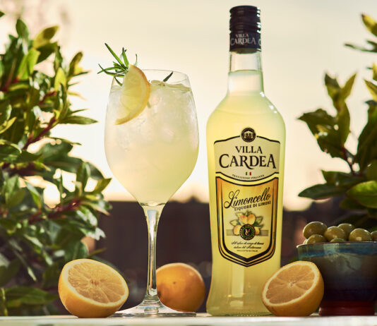 Villa Cardea Limoncello rolls out across Morrisons stores A bottle of Villa Cardea stands next to a wine glass with a Villa Cardea Limoncello Spritz cocktail in it with greenery in the background with oranges around the bottle and serve and a bowl of olives.