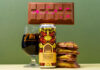A can of Vault City Dubai Style Chocolate Pistachio Imperial Pastry Stout stands on a table with a chocolate bar balanced on top of the can, a glass with the stout inside it to the left of the image and bars of Dubai-Style Chocolate piled up to the right of the can.