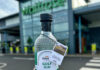 A person is holding a bottle of Eden Mill Golf Gin in front of a Waitrose supermarket store.