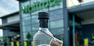 A person is holding a bottle of Eden Mill Golf Gin in front of a Waitrose supermarket store.
