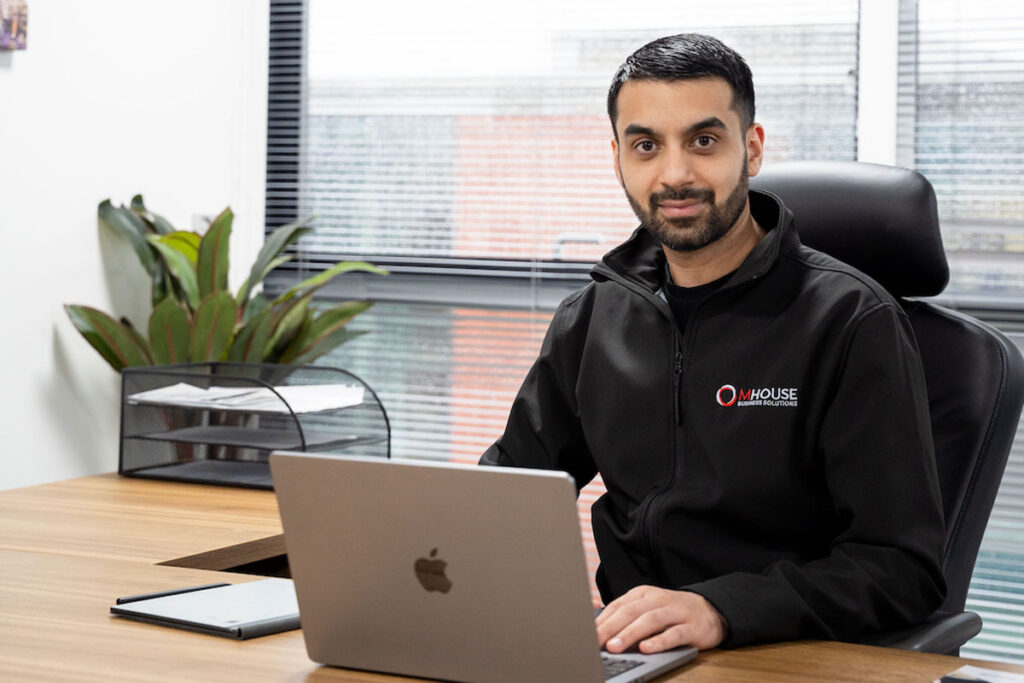 Faisal Sattar, chief executive at MHouse, sits behind a desk with an Apple Mac laptop on it.