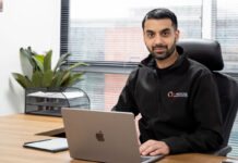 Faisal Sattar, chief executive at MHouse, sits behind a desk with an Apple Mac laptop on it.