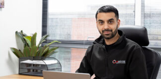 Faisal Sattar, chief executive at MHouse, sits behind a desk with an Apple Mac laptop on it.