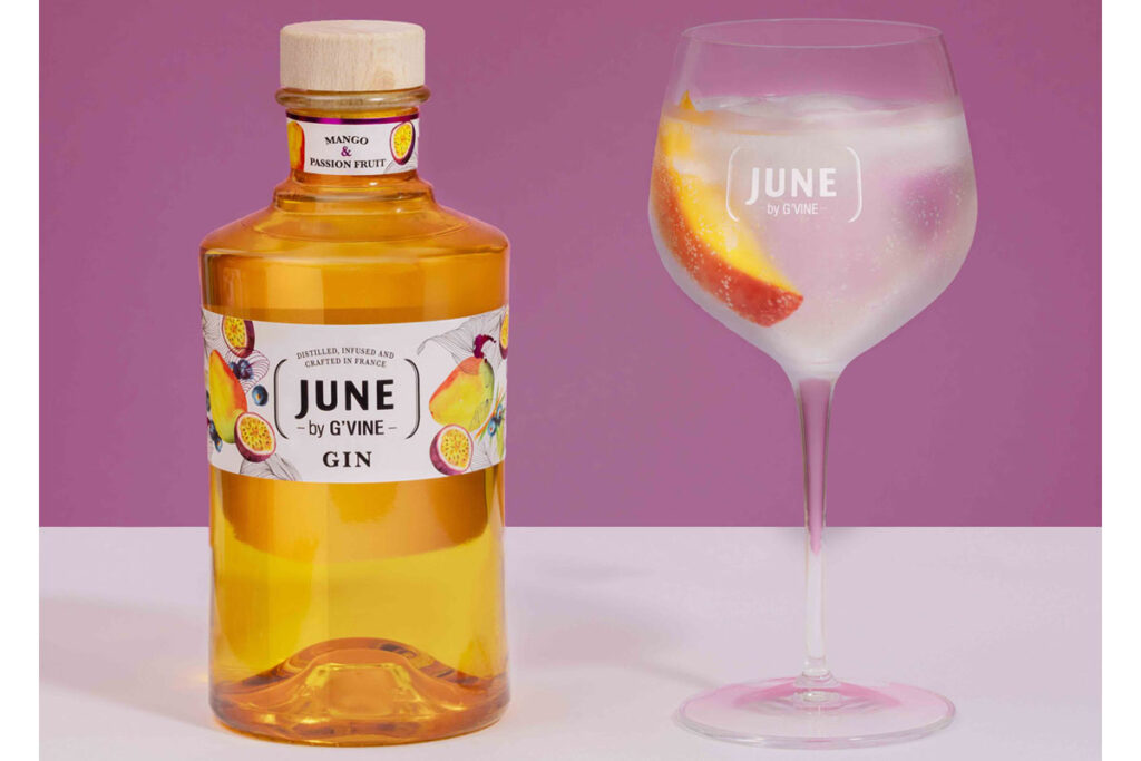 A bottle of June Gin Mango & Passionfruit stands next to a balloon glass with a gin & tonic serve inside it.