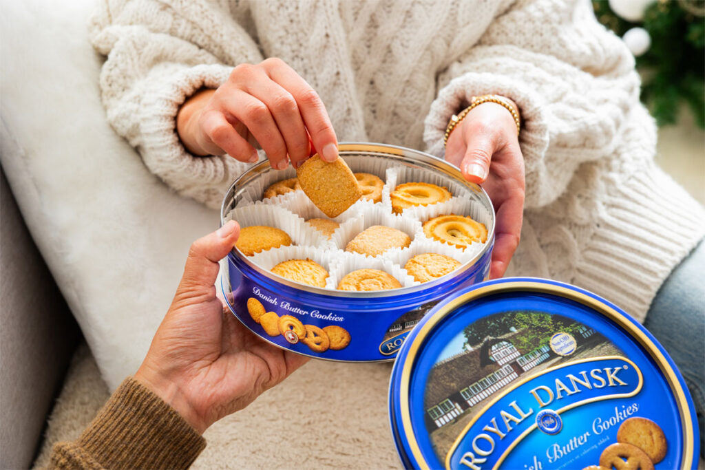 A person lifts biscuits out from a blue Royal Dansk biscuit tin.