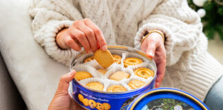 A person lifts biscuits out from a blue Royal Dansk biscuit tin.