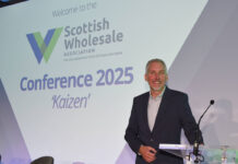 Colin Smith, chief executive at the Scottish Wholesale Association, stands at a podium with the 2025 redesign of the firm's logo behind him.