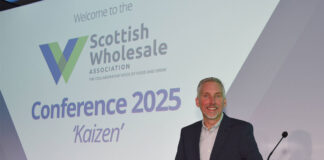 Colin Smith, chief executive at the Scottish Wholesale Association, stands at a podium with the 2025 redesign of the firm's logo behind him.
