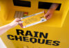 A hand passing out a cheque for £1885 with a Tennent's lager design across the cheque and the ATM machine.