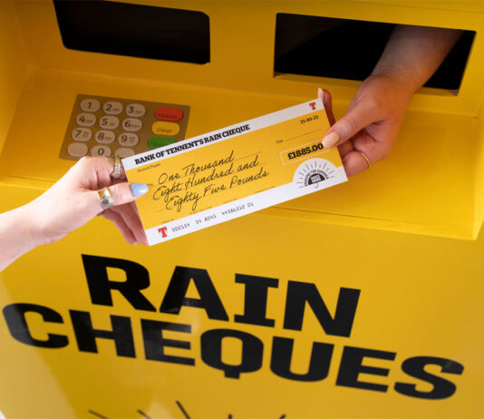 Tennent’s braves the summer with new 140th anniversary campaign A hand passing out a cheque for £1885 with a Tennent's lager design across the cheque and the ATM machine.