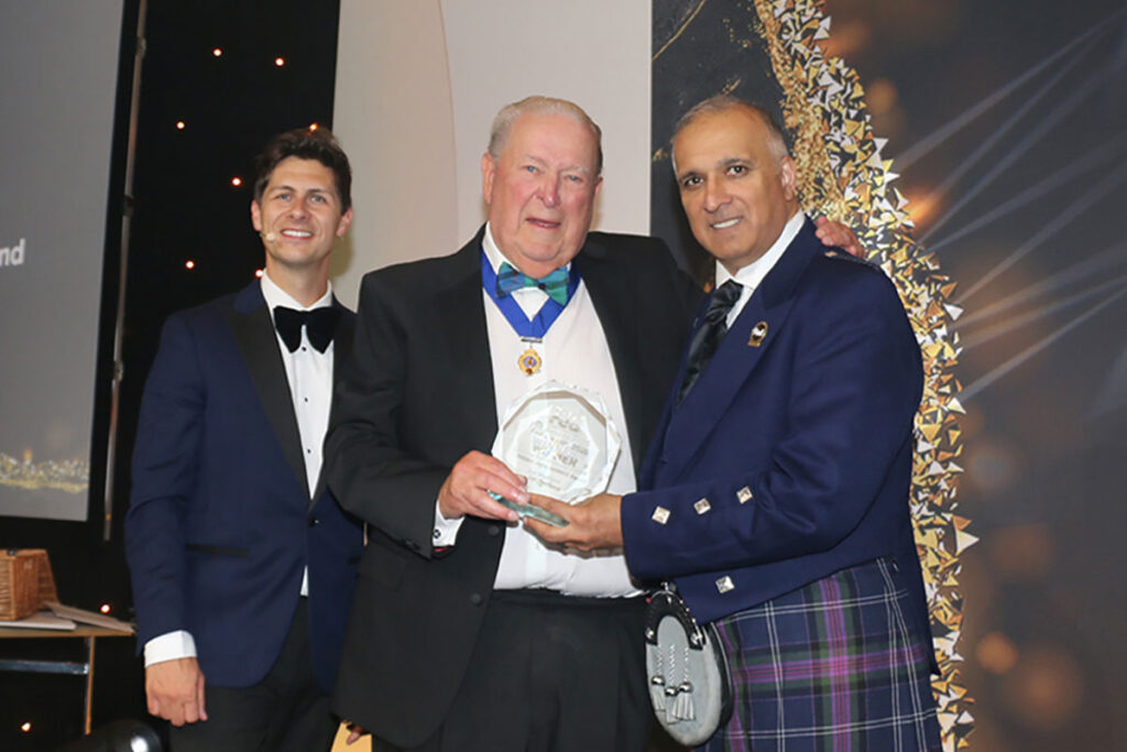 A trio of men stand on a stage at The Fed awards as the Lifetime Achievement Award is handed out.