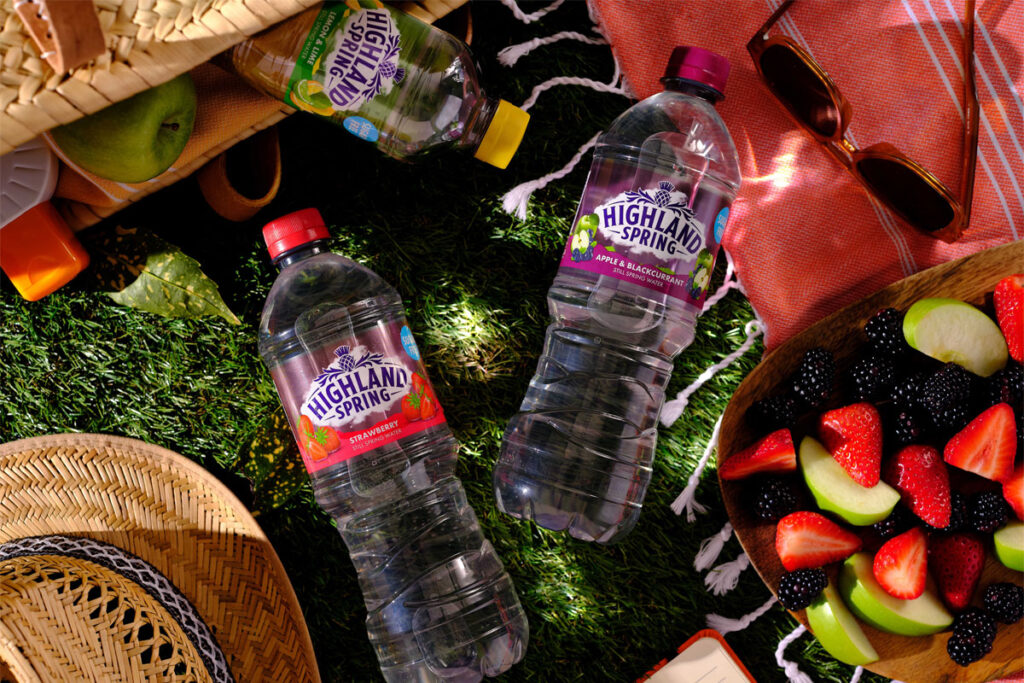 Bottles of Highland Spring flavours water at a picnic with food spilled out onto a patch of grass.